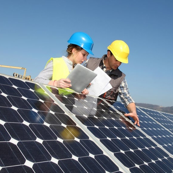 Twee Energy Check medewerkers inspecteren zonnepanelen in het veld met bouwhelmen op.