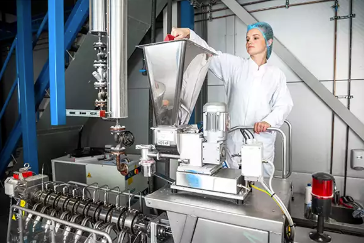 Een medewerker in witte kleding en haarnetje werkt aan een machine in een industriële omgeving bij Energy Check.