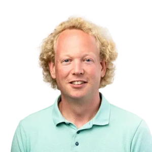 Portret van een lachende man met blond krullend haar in een lichtblauwe polo.